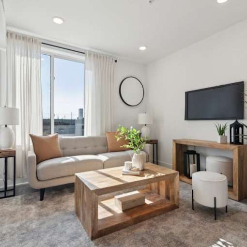A modern living room with a large window, a wooden coffee table, and a flat-screen TV mounted on the wall.