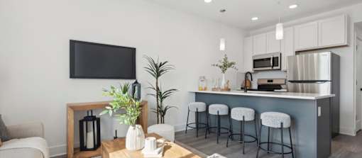 A modern kitchen with a bar stool and a flat screen TV.