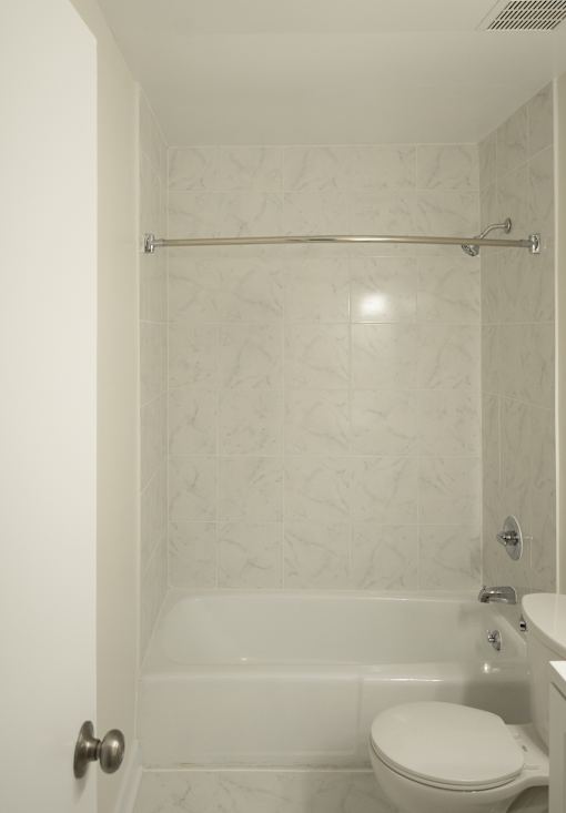 A white toilet is in a bathroom with a marble wall.