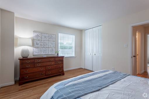 A bedroom with a large bed and a dresser with a lamp on it.