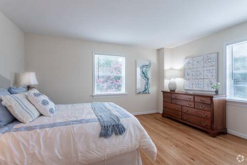 A bedroom with a bed, dresser, and two windows.
