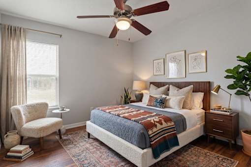 A bedroom with a bed, chair, and ceiling fan.