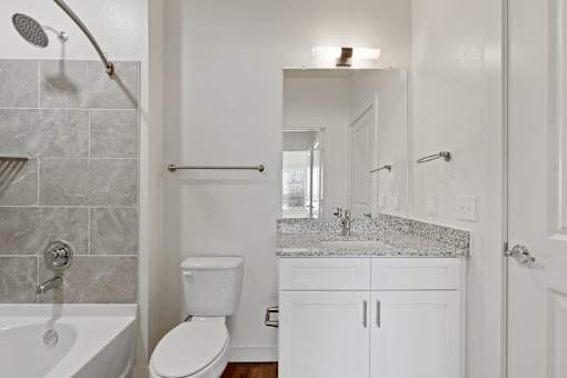 A white bathroom with a marble counter top and a white toilet.