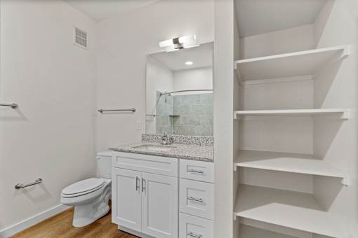 A white bathroom with a toilet, sink, and shelves.