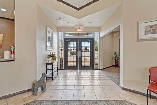 A hallway with a dog statue on the floor and a red chair on the right side.