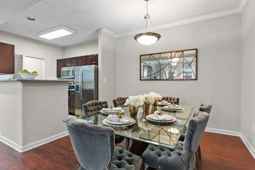 A dining room with a glass table and grey chairs.