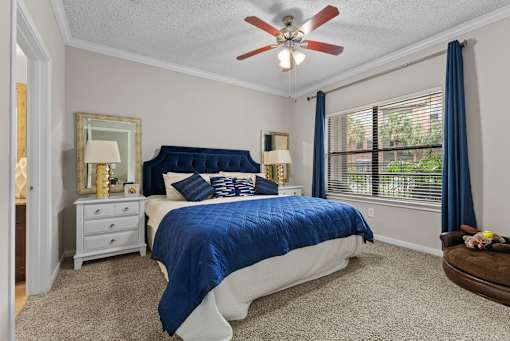 A bedroom with a blue bedspread and a ceiling fan.