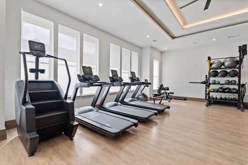 A spacious gym with treadmills, elliptical machines, and a rack of dumbbells.