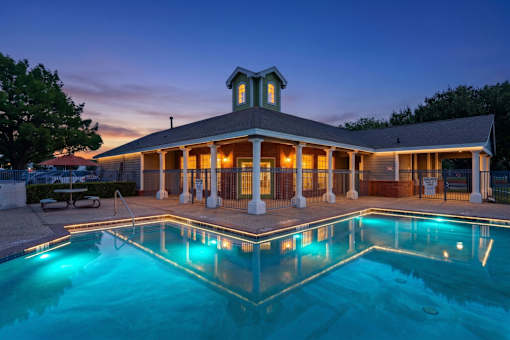 A pool in front of a house with lights on.