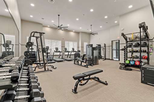 A spacious gym with a variety of equipment including dumbbells, weight machines, and a bench.