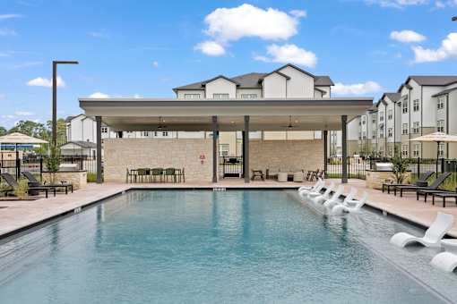 A large swimming pool in front of a building with a covered seating area.