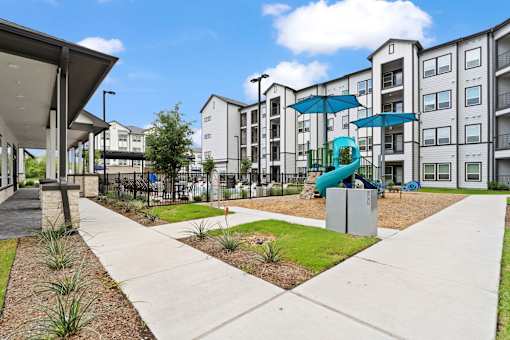 A modern apartment complex with a playground and a fence.