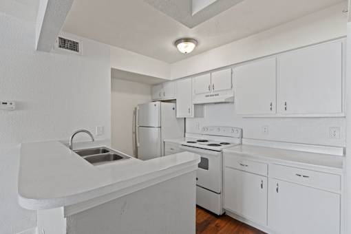 A white kitchen with a stove, refrigerator, and sink.