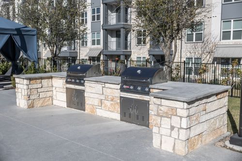 Three stone BBQs are lined up in a row. at Enclave on Ross Apartments, Del Valle, Texas
