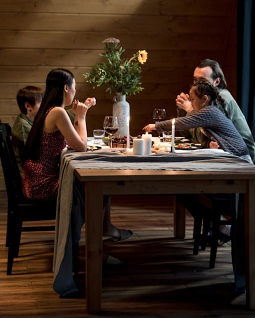 A family is sitting at a wooden table with a vase of flowers in the middle at Enclave on Ross Apartments, Del Valle, TX
