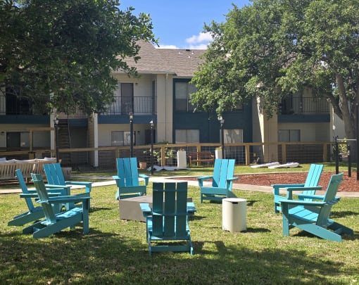 an outdoor lounge area with chairs and trees in front of an apartment building