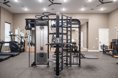A gym with a variety of equipment including treadmills, weights, and a squat rack. at Enclave on Ross Apartments, Del Valle, TX, 78617
