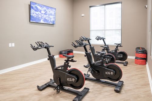 A room with exercise bikes and a TV mounted on the wall. at Enclave on Ross Apartments, Del Valle, Texas