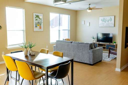 A dining table with yellow chairs in a room with a grey couch.