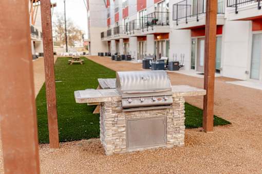A BBQ grill is in the middle of a gravel area.
