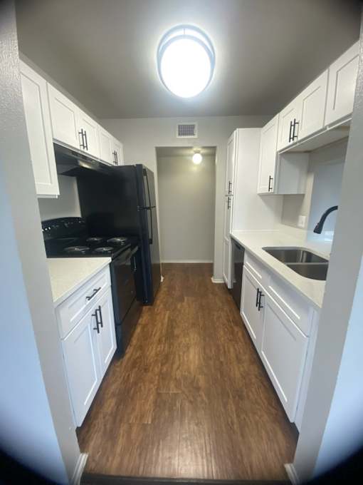 a kitchen with white cabinets and black appliances and a wood floor