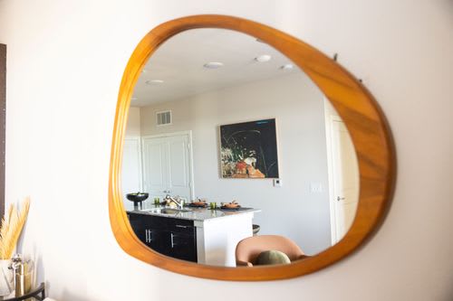 A round mirror with a wooden frame hangs on a wall. at Enclave on Ross Apartments, Del Valle, TX