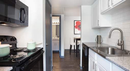 A black stove top oven sits in a kitchen with white cabinets and a red flower picture on the wall.