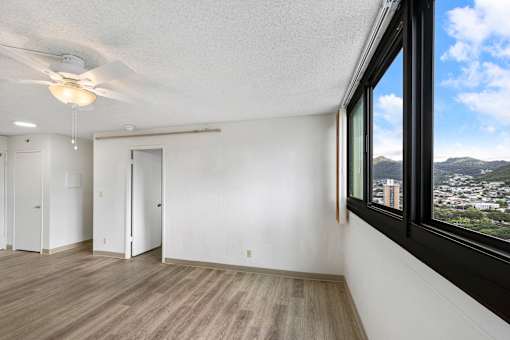 A room with a ceiling fan and a window overlooking a cityscape.