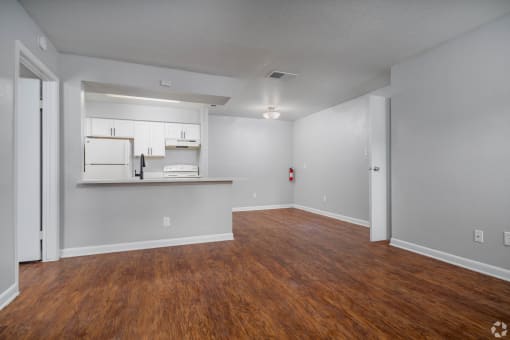 the living room and kitchen of an apartment with wood flooring and white cabinets
