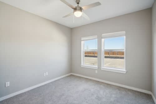 A room with a ceiling fan and two windows.