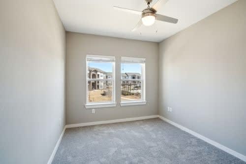 A room with a ceiling fan and two windows.