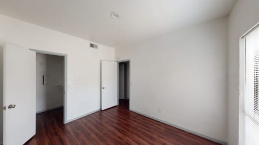 a bedroom with white walls and wood floors and a closet