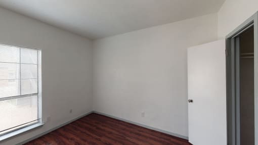 a bedroom with white walls and wood flooring and a window
