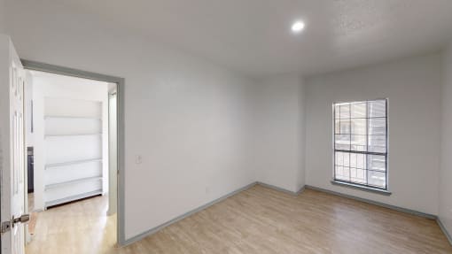 a bedroom with white walls and wood flooring and an open door to a closet
