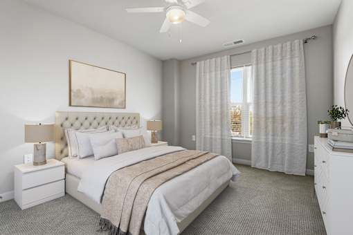 A bedroom with a large bed, a ceiling fan, and a window with curtains.