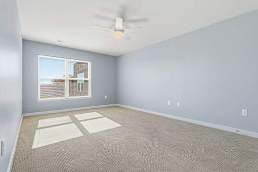 A room with a ceiling fan and a window overlooking a building.