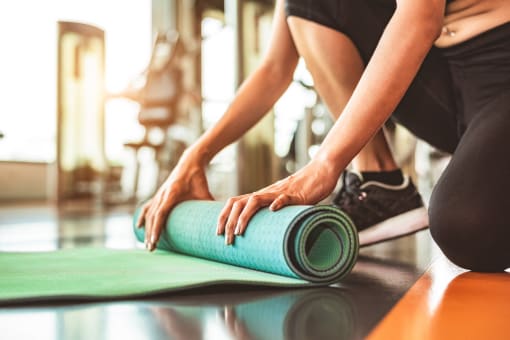 a woman rolling up a yoga mat in a gym
