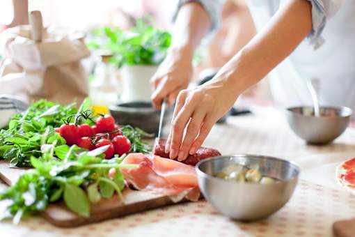 A person is slicing meat on a cutting board with fresh vegetables and herbs around.