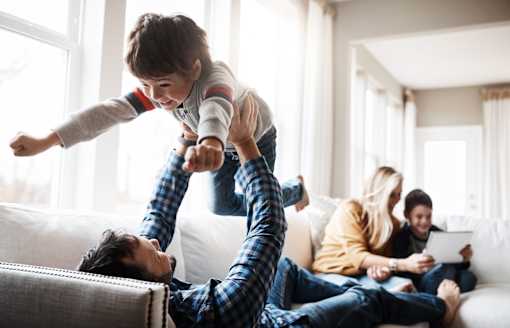 A man is lying on the couch with a child on his feet.