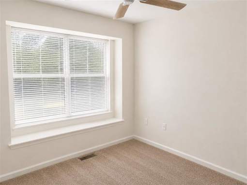 A room with a window covered in blinds and a ceiling fan.