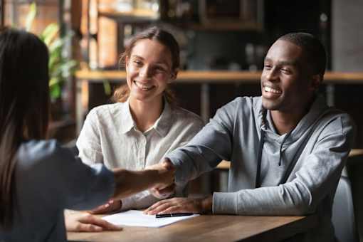 Two people shaking hands over a document at a table.