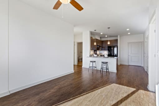 a living room with white walls and a kitchen in the background