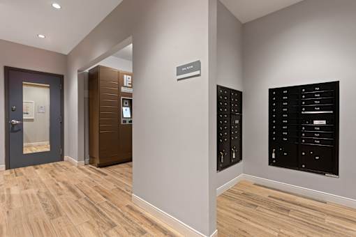 A hallway with a black control panel on the wall and a wooden floor.