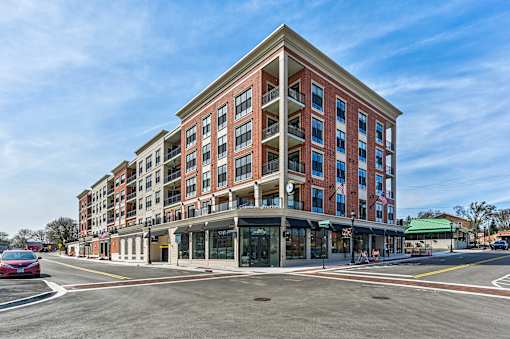 A red car is parked on the side of the road in front of a multi-story building.