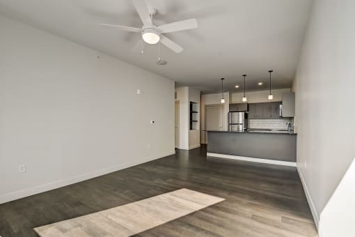 an empty living room with a ceiling fan and a kitchen in the background