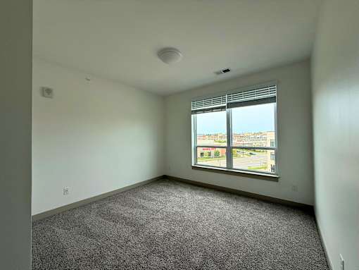 A room with a carpeted floor and a window overlooking a parking lot.