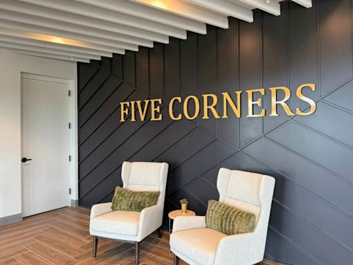 Two white chairs are placed in front of a wall with the name "FIVE CORNERS" written on it.