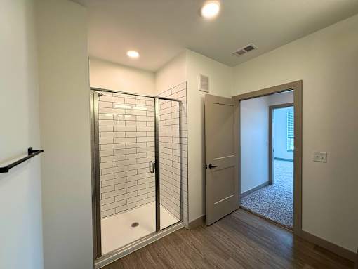 A bathroom with a glass shower door and a wooden floor.