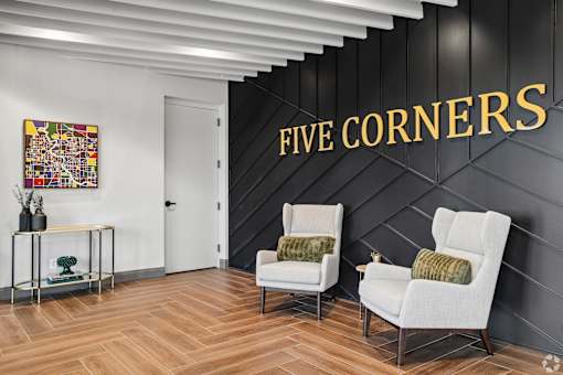Two white chairs are placed in front of a black wall with the words "FIVE CORNERS" written on it.
