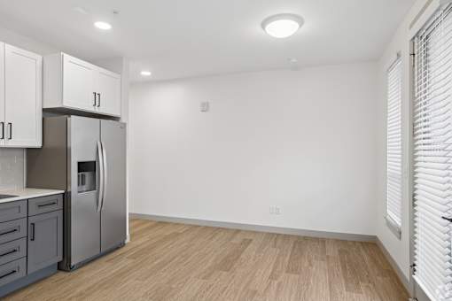 A kitchen with a refrigerator, cabinets, and a wooden floor.